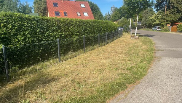 A residential area with a red-roofed house, a metal fence, and a paved road. - Rauchfangswerder Holiday Home with Private Terrace, Garden, and Wi-Fi (Berlin)