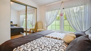 A bedroom with a bed, a chair, a large mirror, and a window with curtains. - Rauchfangswerder Holiday Home with Private Terrace, Garden, and Wi-Fi (Berlin)