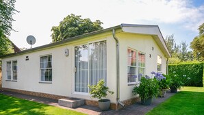 A single-story house with a white exterior, a satellite dish, and a small garden with potted plants and flowers. - Rauchfangswerder Holiday Home with Private Terrace, Garden, and Wi-Fi (Berlin)