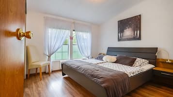 Ein Schlafzimmer mit einem Bett, einem Sessel, einem Nachttisch und einem Fenster mit Vorhängen.