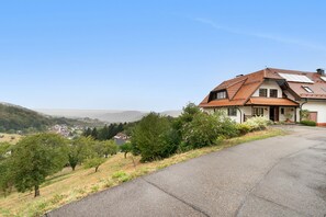 A house with a sloped roof, a paved driveway, and a view of a valley with houses and trees. - Nasdala Holiday Apartment: Relax with Stunning Panoramic Views (Bühlertal)