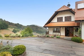 A two-story house with a sloped roof, a front porch, and a view of a hilly landscape.