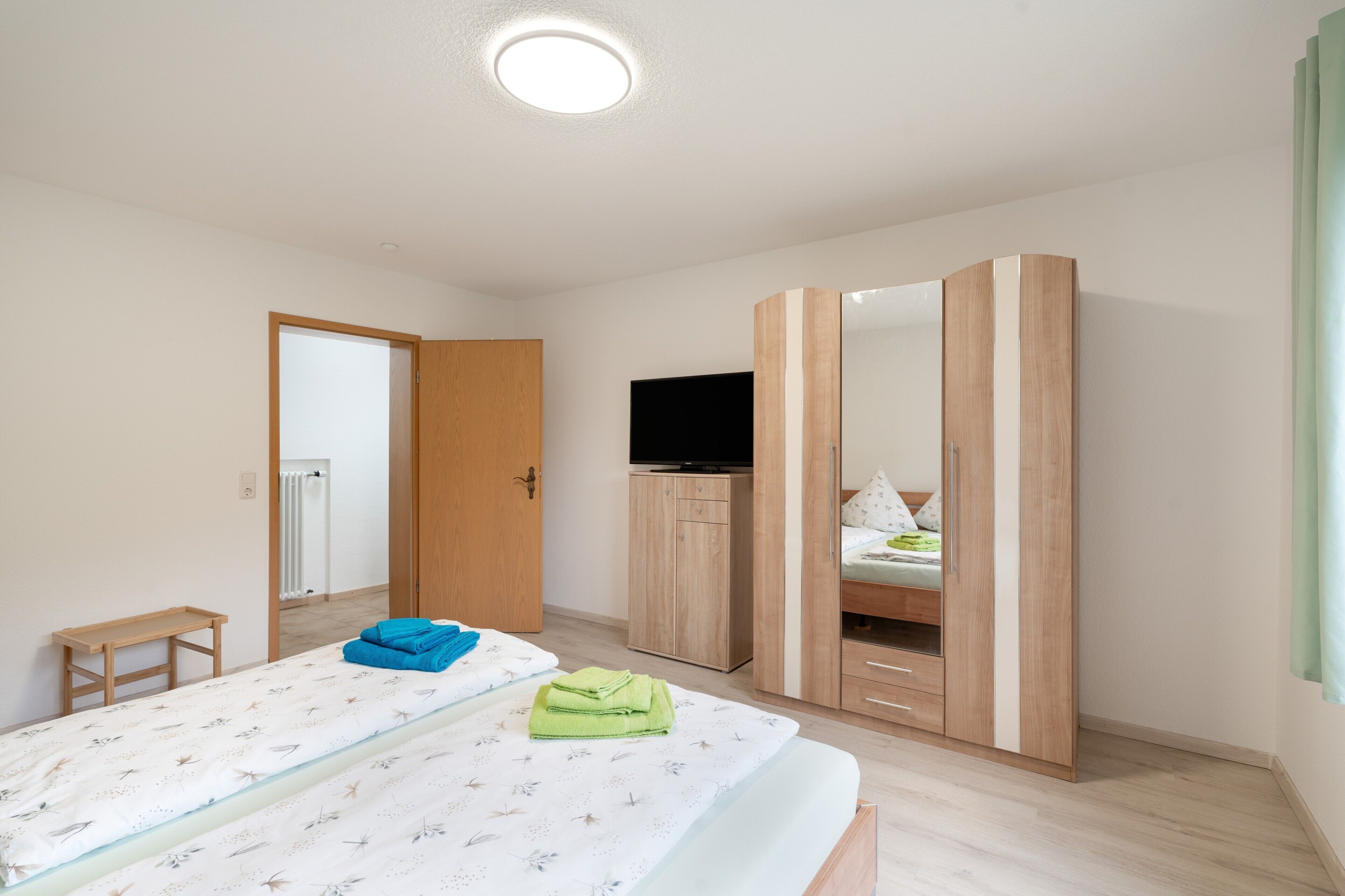 Un dormitorio con cama, televisión, armario y una pequeña mesa.