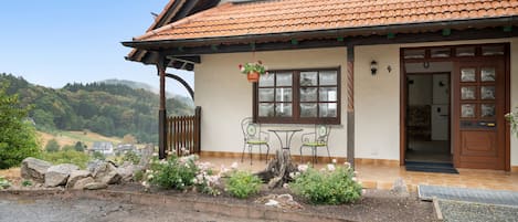A two-story house with a tiled roof, a porch with a bench, and a view of the surrounding landscape.