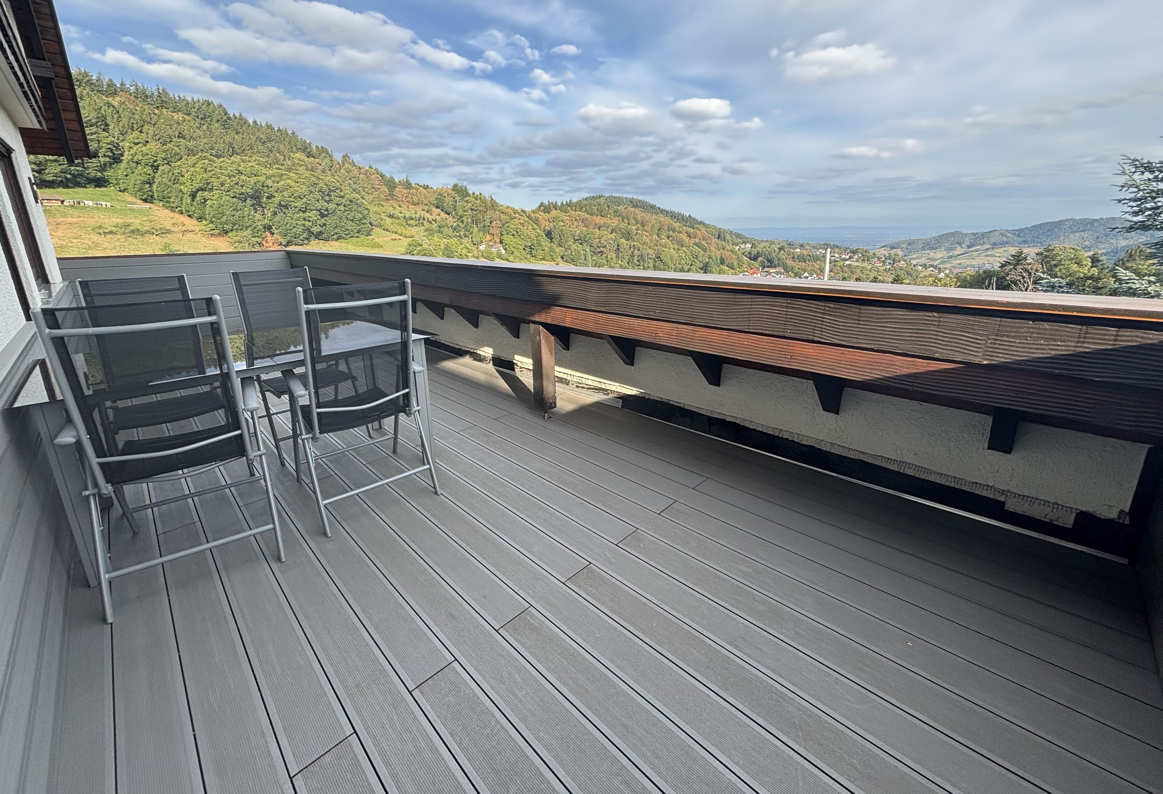 Una terraza con mesa y sillas de vidrio, con vista a un paisaje montañoso.