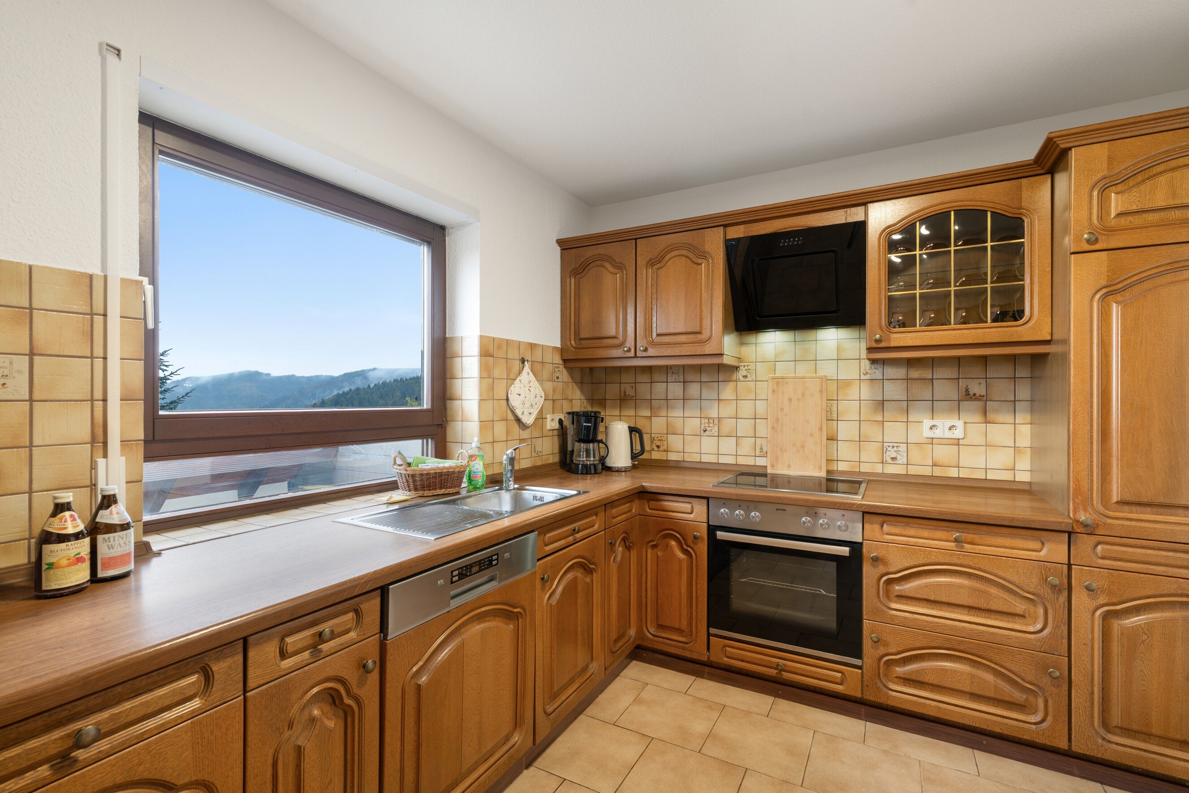 Una cocina con armarios de madera, lavavajillas, horno y ventana con vista a las montañas.