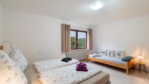 A bedroom with two beds, a window with curtains, a bedside table with a lamp, and a radiator.