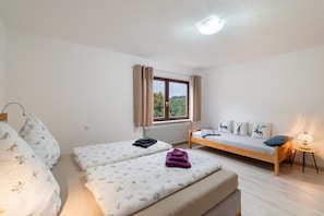 A bedroom with two beds, a window with curtains, a bedside table with a lamp, and a radiator.