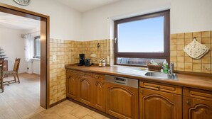 A kitchen with wooden cabinets, a built-in dishwasher, a window, and a clock on the wall.