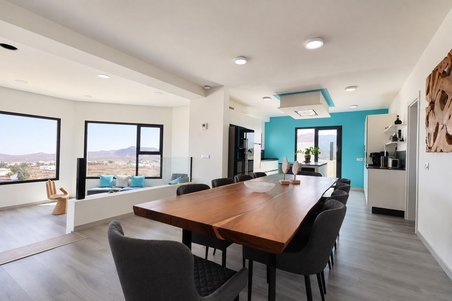 Un comedor moderno con una mesa larga, varias sillas y vistas del paisaje a través de ventanas amplias.