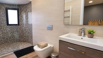 Un baño moderno con ducha, inodoro, lavamanos y espejo.