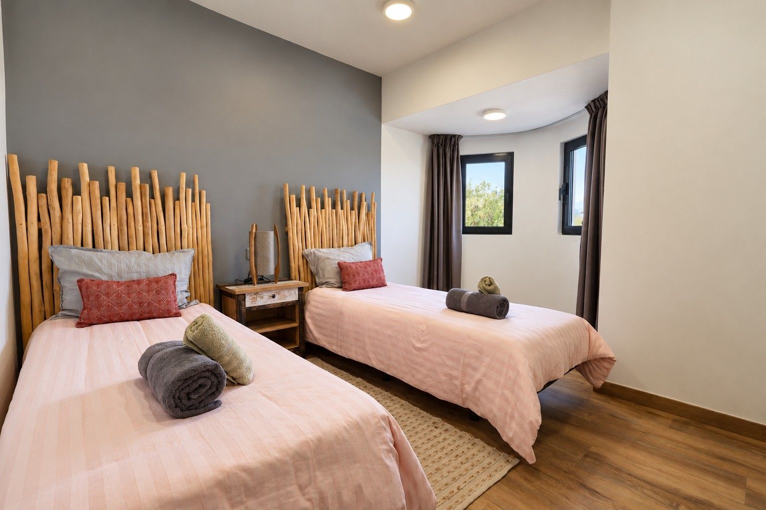 Habitación de hotel con dos camas, cabecero de madera, mesita de noche y ventana con cortinas.