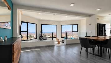 A modern kitchen with large windows, a dining area with a wooden table, and a view of the landscape.