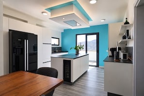 A modern kitchen with a central island, white cabinetry, a black refrigerator, and a blue accent wall. - Vacation villa 'Exceptionnelle avec piscine' with sea view, private pool and Wi-Fi (Villaverde)