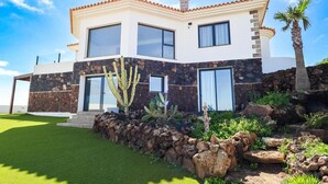 A modern two-story house with a stone facade, large windows, and a well-maintained garden with cacti and rocks.