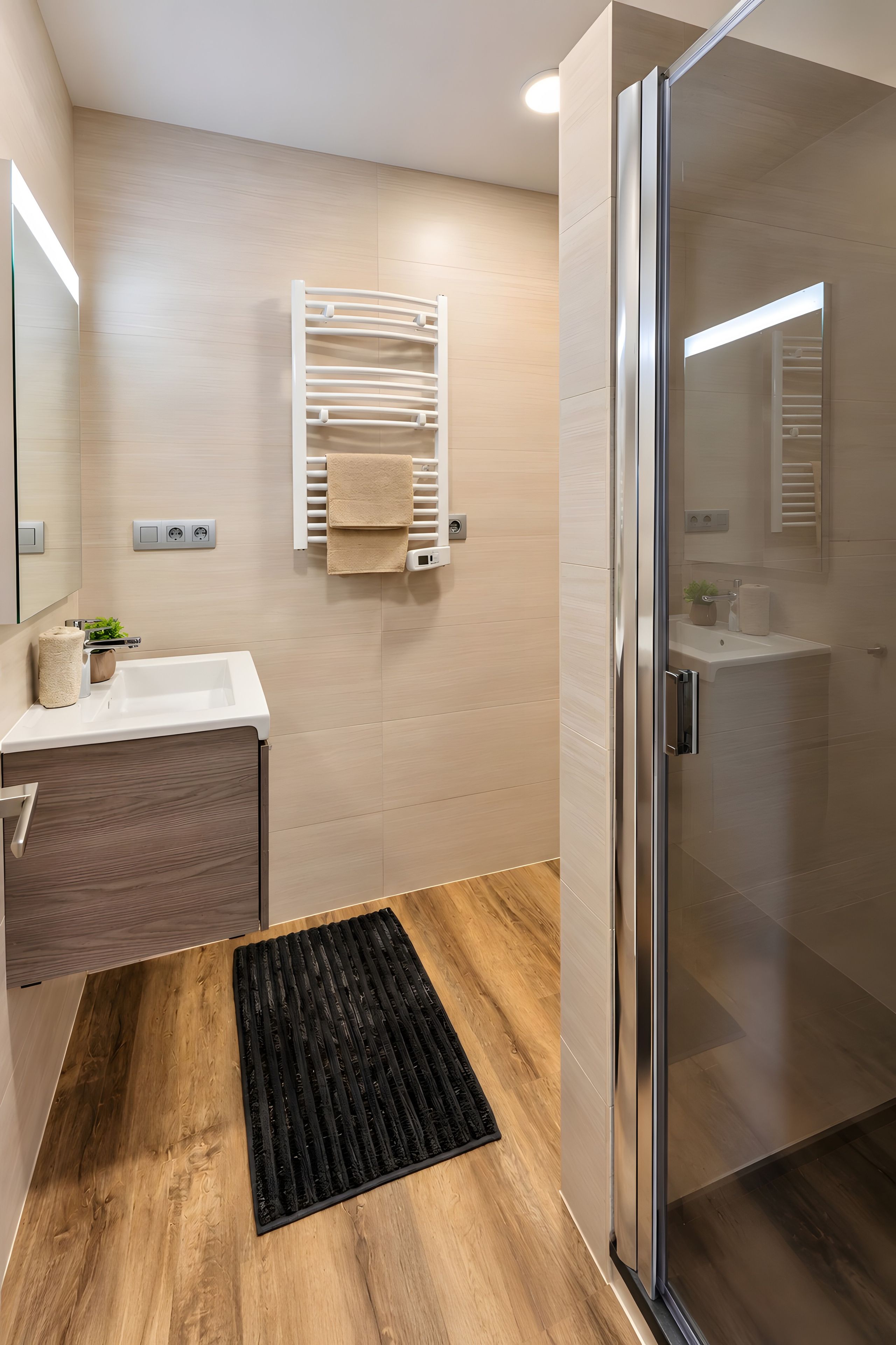A modern bathroom with a glass shower enclosure, a white sink, and a towel rack.