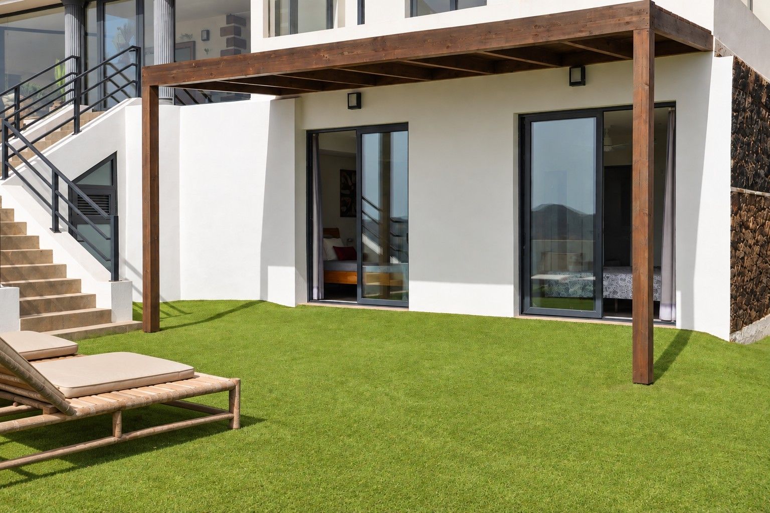 Et moderne hus med en overdækket terrasse, en trappe og en velplejet græsplæne.