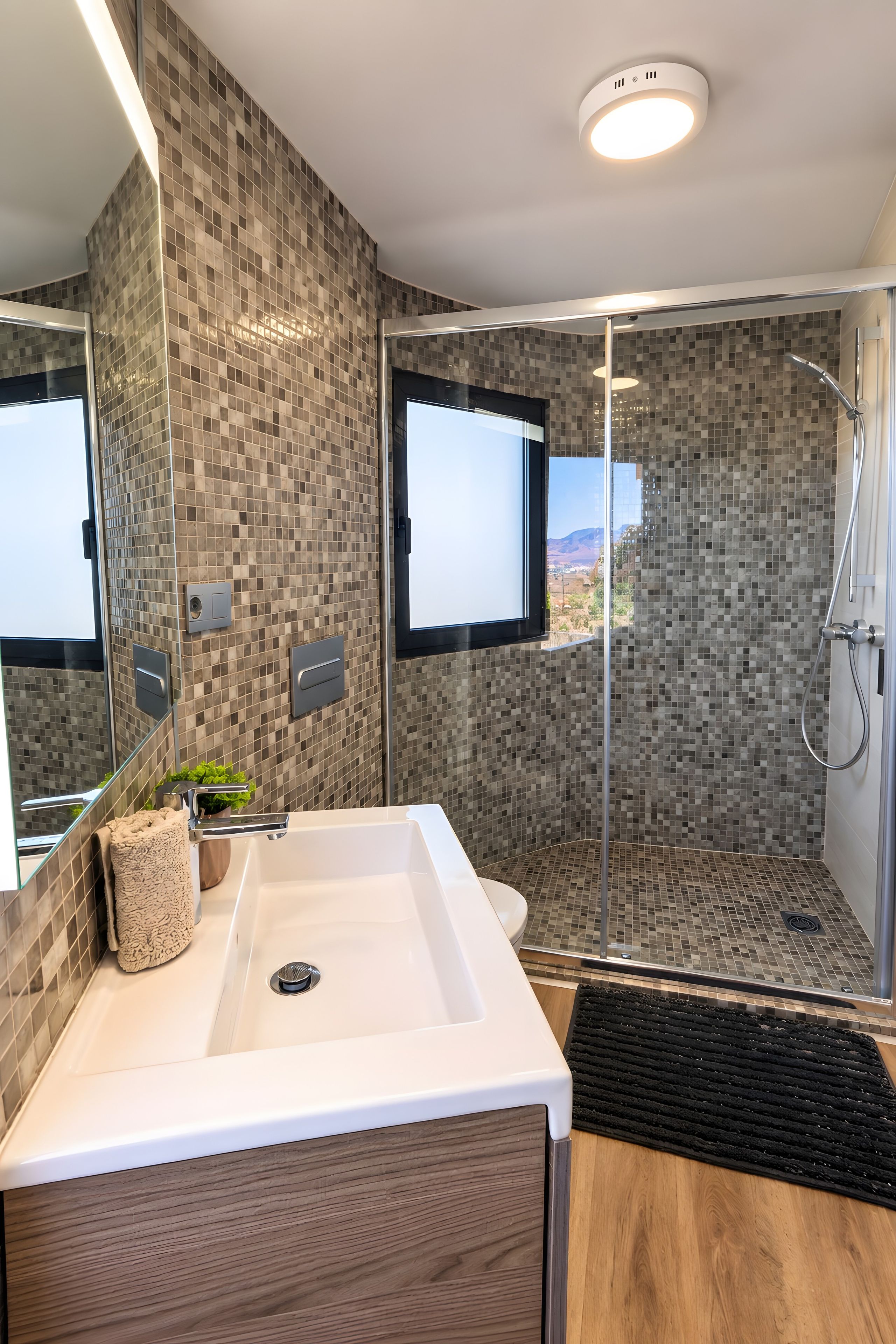 Een moderne badkamer met een grote spiegel, een wastafel en een douche met uitzicht op de omgeving.
