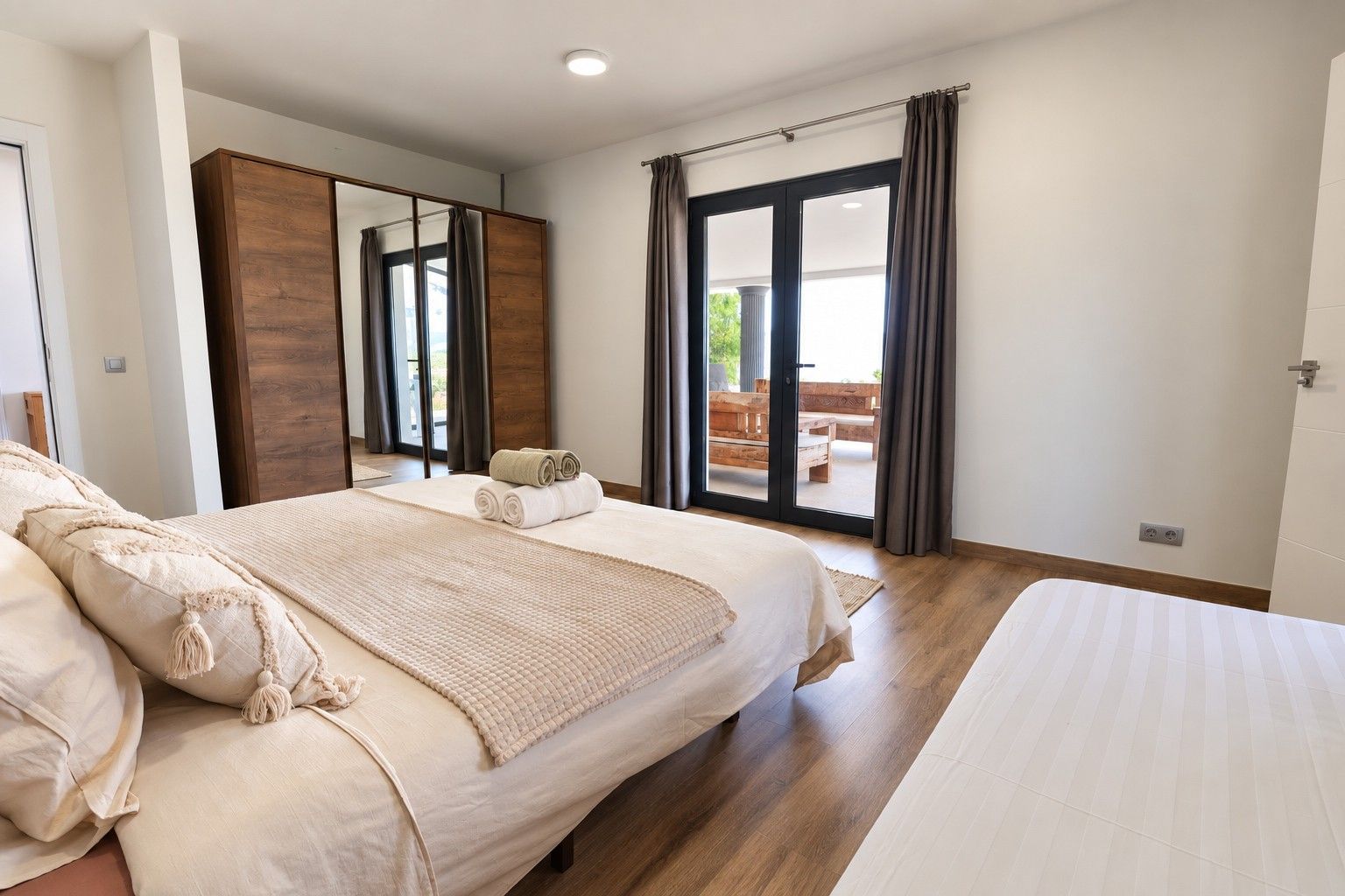 Un dormitorio con una cama grande, un armario de madera, una puerta corrediza de vidrio a un balcón y un espejo amplio.