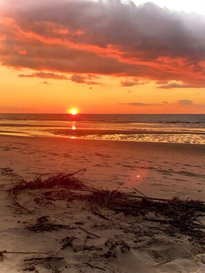 Una playa con el sol poniéndose sobre el horizonte, creando un reflejo en el agua.