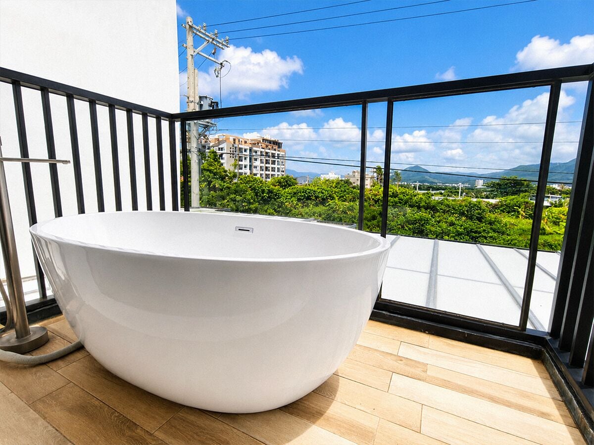 Uma casa de banho moderna com uma banheira independente, soalho em madeira e varanda com vista para edifícios e vegetação.