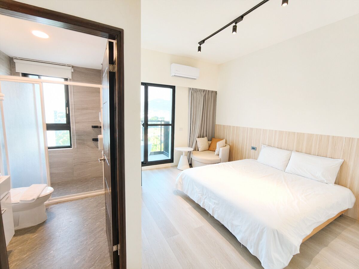 A hotel room with a bed, a sofa, a small table, and a bathroom with a toilet and shower.