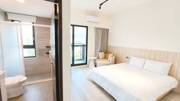 A hotel room with a bed, a sofa, a small table, and a bathroom with a toilet and shower.