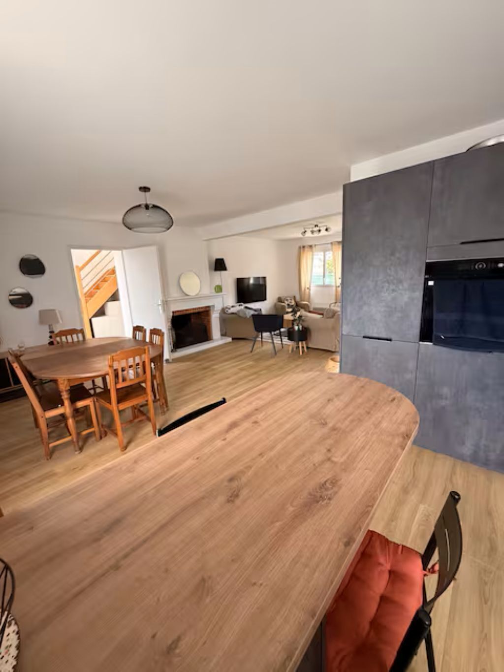 Eine moderne Küche mit Backofen, ein Essbereich mit Holztisch und -stühlen sowie ein Wohnbereich mit Sofa und Fernseher.