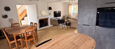 Eine moderne Küche mit Backofen, ein Essbereich mit Holztisch und -stühlen sowie ein Wohnbereich mit Sofa und Fernseher.