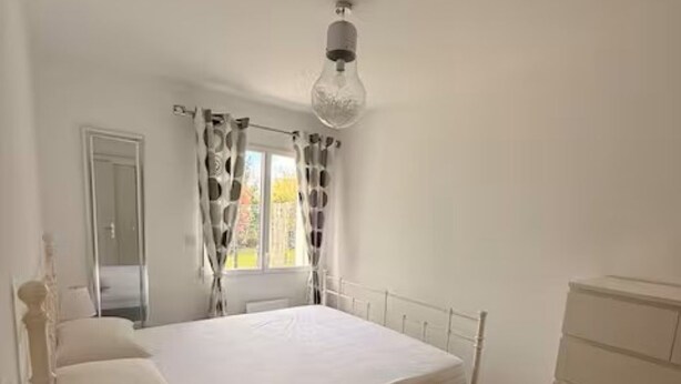Um quarto com uma cama, penteadeira, abajur e janela com cortinas.