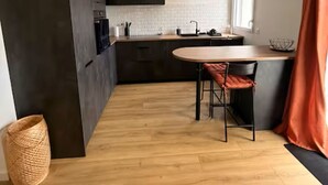 Uma cozinha moderna com uma mesa de jantar redonda, armários escuros e uma janela com cortinas.