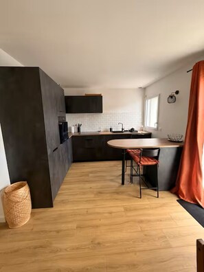 Eine moderne Küche mit einem runden Esstisch, dunklen Schränken und einem Fenster mit Vorhängen.