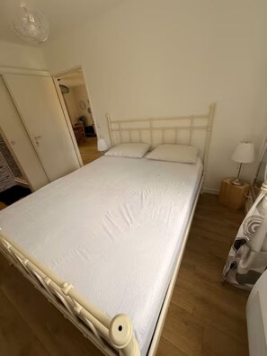 Habitació individual amb un llit i capçalera de fusta, una taula de nit amb una làmpada i un armari.
