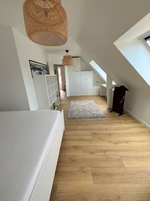 A spacious attic room with a sloped ceiling, wooden flooring, a large window, and a woven light fixture. - Single-family home near amenities (Arzon)