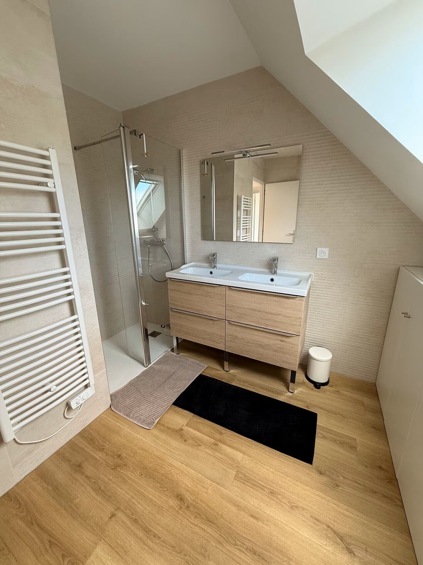 Een moderne badkamer met een douche, een wastafel met spiegel en een zwart vloerkleed.