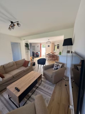 A modern living room with a sofa, armchair, and coffee table. There is a dining area in the background with a table and chairs. - Single-family home near amenities (Arzon)