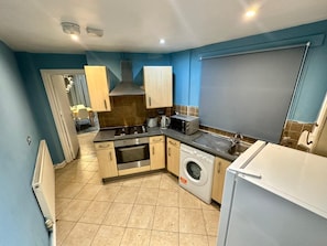 A compact kitchen with a stove, oven, microwave, toaster, sink, and a washing machine. - The London Stage Door (London)