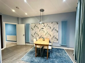 A dining area with a wooden table and chairs, a patterned wallpaper, and a radiator. - The London Stage Door (London)
