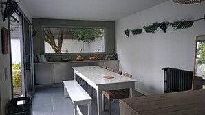 A dining area with a white table and benches, a window with a view of trees, and a radiator on the wall. - A Little Paradise with a Pool in the Heart of Nantes (Nantes)