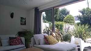 A modern living room with a sofa, a coffee table, and a view of a garden through large windows. - A Little Paradise with a Pool in the Heart of Nantes (Nantes)