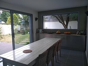 A dining area with a table and chairs, a window with a view of greenery, and a shelf with books and decorative items. - A Little Paradise with a Pool in the Heart of Nantes (Nantes)
