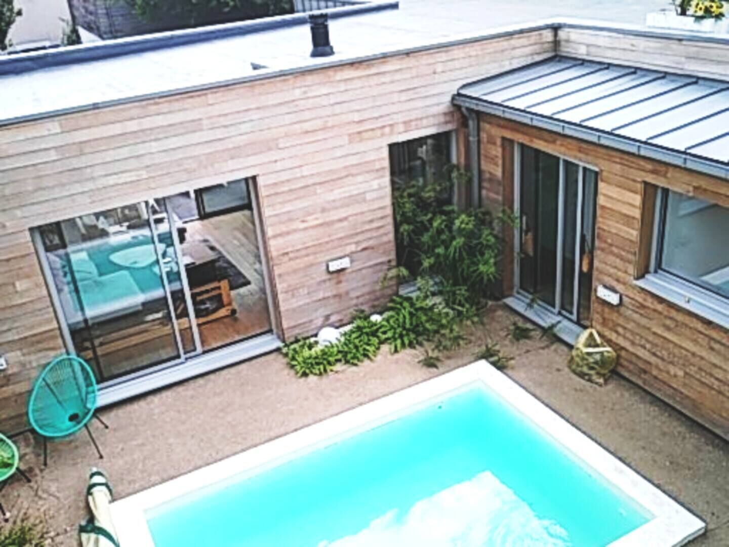 Una casa moderna con piscina, un patio con una silla y un ventanal de vidrio que da a una habitación.