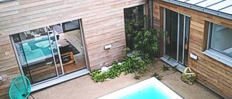 Una casa moderna con piscina, un patio con una silla y un ventanal de vidrio que da a una habitación.