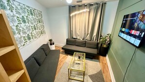 Una sala de estar con sofá, una mesa de centro, un televisor montado en la pared y una planta.