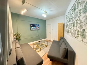 A living room with a sofa, a coffee table, a television mounted on the wall, and a large botanical wallpaper. - The Borough Base (London)