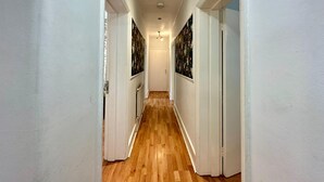 Un pasillo con piso de madera, paredes blancas y puertas con papel tapiz floral.