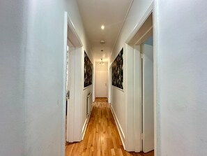 A hallway with wooden flooring, white walls, and doors with floral wallpaper. - The Borough Base (London)
