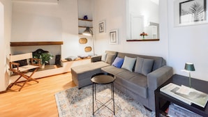 Una sala de estar moderna con un sofá gris, una mesita redonda, suelo de madera y una estantería llena de libros.