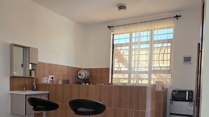 A kitchen with two bar stools, a refrigerator, and a window with curtains. - MIHAMBOS RESIDENCE (Msambweni)