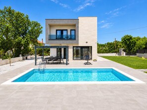 Una casa moderna de dos pisos con piscina, muebles de exterior y un patio cubierto.